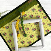 Embroidery hoop with yellow and green thread on a floral fabric mat